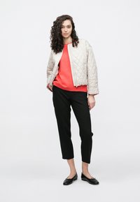 Pikowana jasnoszara kurtka bomberka, pomarańczowy sweter, czarne krótkie spodnie i czarne baleriny. Kurtka ma zapięcie na zamek i ściągacze przy rękawach.