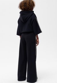 Czarna, krótka bluza z kapturem i szerokimi rękawami, zestawiona z czarnymi spodniami o wysokim stanie z białymi paskami po bokach. Miękka tekstura.