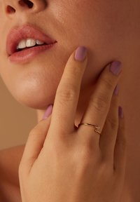 Bague en or avec deux petites pierres exposée sur une main à la peau douce et au vernis à ongles lavande, soulignant un look naturel.