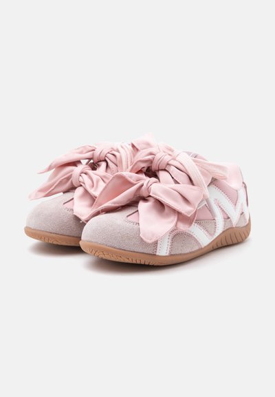 Paire de baskets roses en daim et tissu avec de grands nœuds en ruban satin et des bandes blanches en accent sur des semelles en caoutchouc marron.