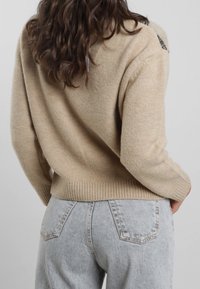 Pullover a maglia beige con vestibilità ampia, orlo e polsini a coste, tessuto testurizzato, abbinato a jeans grigio chiaro a vita alta.