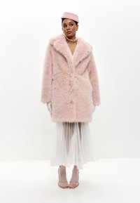 Rosa faux fur frakke med sjalkrave, lange ærmer og knaplukning foran, parret med en gennemsigtig hvid nederdel og lyserøde hæle.