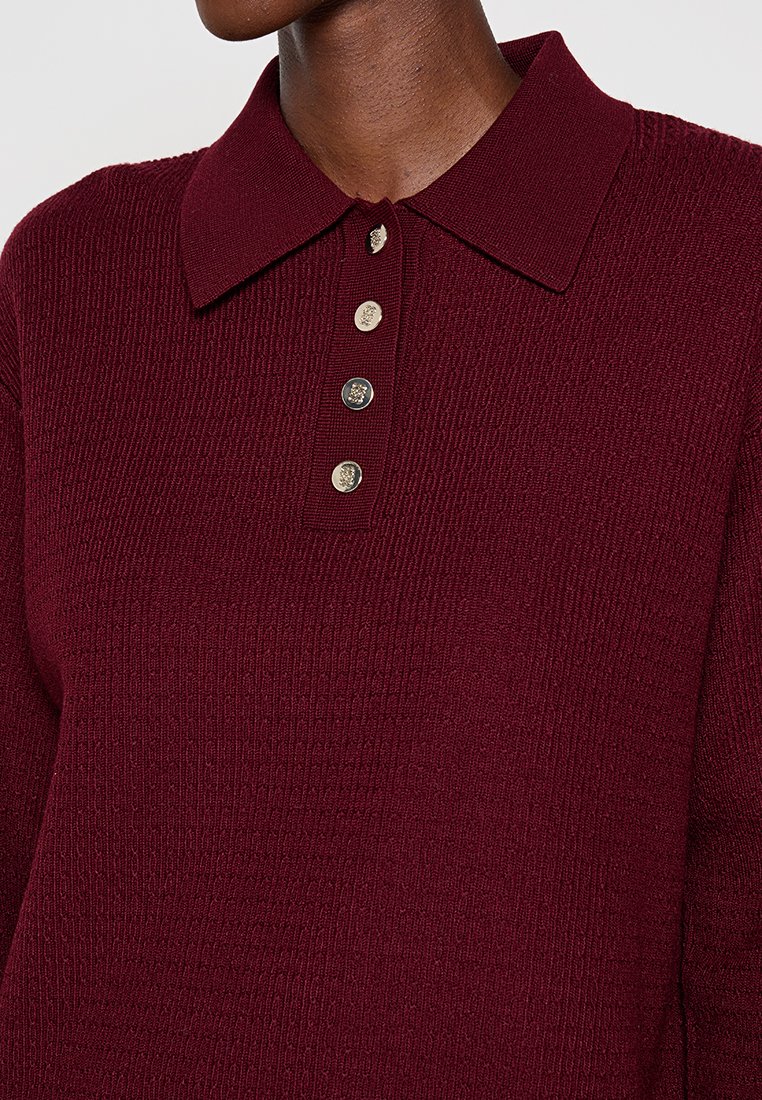 Maglione polo in maglia bordeaux con tessuto testurizzato, colletto classico e quattro bottoni metallici sul davanti.