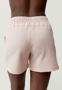 Svetloružové športové šortky vyrobené z textúrovanej látky. Obsahujú elastický pás a bočné vrecká, majú voľný strih a zakončené okraje.