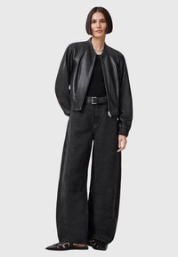 Giacca bomber nera in pelle con colletto a coste, silhouette oversize e zip elegante; abbinata a pantaloni neri a gamba larga a vita alta.