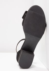 Sandale noire à petit talon bloc vue par le dessous avec une semelle texturée antidérapante.