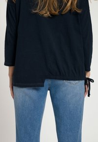Navyblauwe pullovertop met driekwartmouwen en zijknoopjes. Gecombineerd met lichtblauwe denim jeans met een iets taps toelopende pasvorm.