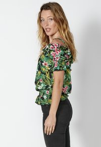 Top floreale off-shoulder con sfondo nero, foglie verdi e fiori rosa e bianchi. Finitura a volant con elastico all'orlo.