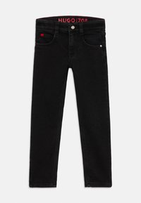 Jean en denim noir avec une coupe slim, design à cinq poches et quincaillerie en métal. La taille présente une étiquette logo rouge pour la marque.