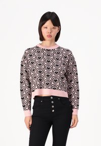 Maglione corto nero e rosa con motivo a cuore, con scollatura e polsini a coste, abbinato a jeans neri a vita alta con dettagli botones.
