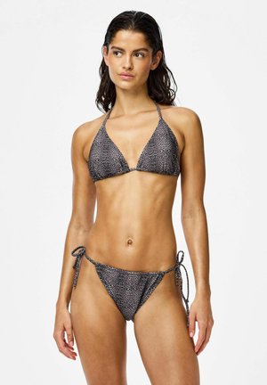 Femme aux cheveux mouillés portant un bikini triangle imprimé léopard gris et noir, posant sur un fond blanc uni.
