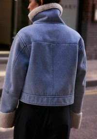Giubbotto di jeans con design cropped, di colore azzurro chiaro, e colletto e polsini in shearling. Presenta cuciture a vista e dettaglio sul retro.