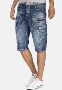 Shorts cargo en denim bleu clair, dotés de plusieurs poches, de détails zippés et d'un motif usé. Fini avec un ourlet à revers.