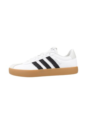 Baskets basses Adidas blanches avec trois bandes noires et semelle en gomme, vues de profil.