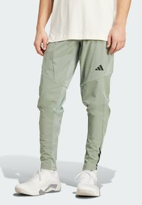 Jasnozielone spodenki sportowe o zwężanym kroju, z czarnymi akcentami i logo Adidas. Wykonane z gładkiego, elastycznego materiału.