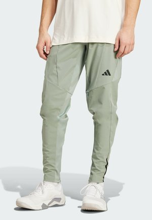 Light green athletic pants with a tapered cut, featuring black accents and an Adidas logo. Made of a smooth, stretchy material.