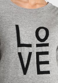 Šedý svetr s kulatým výstřihem, na kterém jsou výrazné černé písmena tvořící slovo "LOVE", vyznačuje se jemnou pletenou texturou.