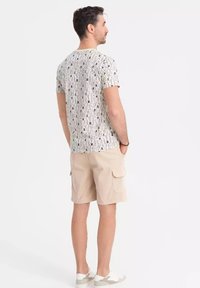 Chemise à manches courtes avec un motif noir et blanc. Portée avec un short cargo beige et des chaussures légères à enfiler.