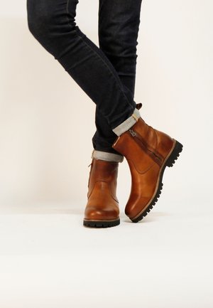 Bruine leren enkellaarsjes met een gestructureerde afwerking, een zijrits en een zwarte rubberen zool, gecombineerd met opgerolde donkere jeans.