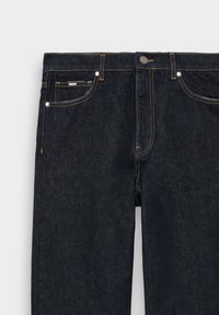 Jean en denim foncé avec une texture lisse, comportant des coutures jaunes, cinq poches et une fermeture à bouton en métal.