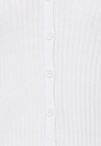 Vit stickad cardigan med ribbad textur och sex matchande knappar framtill.