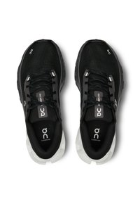 Baskets de sport noires avec un dessus en maille texturée, présentant un accent blanc sur la semelle et des lacets noirs. Logo visible sur la languette et sur le côté.