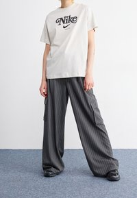 Světle béžové bavlněné tričko má černé logo Nike. Šedé kárované cargo kalhoty mají boční kapsy a volný střih. Celkový vzhled dotvářejí černé tenisky.