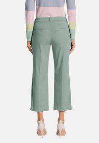 Lichtgroene wijde broek met achterzakken, gecombineerd met een gestreepte multicolore trui. De broek heeft een gladde textuur en een getailleerde pasvorm.