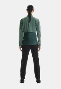 Jachetă sport ușoară, verde, cu un design scurt, asortată cu pantaloni negri cu fermoare. Textură netedă cu accente practice.