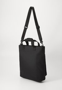 Sac en tissu noir avec une sangle réglable, deux poignées supérieures, forme rectangulaire, design minimaliste et sans matériel ni motifs visibles.
