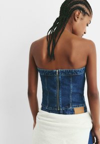 Top fără bretele din denim albastru, cu închidere cu fermoar la spate, având un design ajustat și o pată bej la linia taliei.