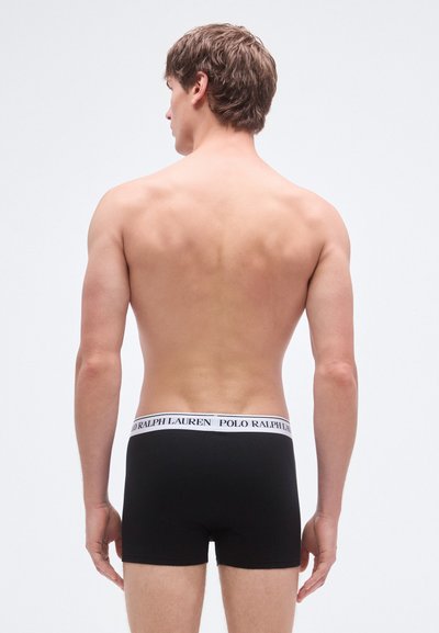 Cuecas boxer pretas com cintura branca apresentando o texto "POLO RALPH LAUREN." Feitas de tecido suave, design ajustado e comprimento até a metade da coxa.
