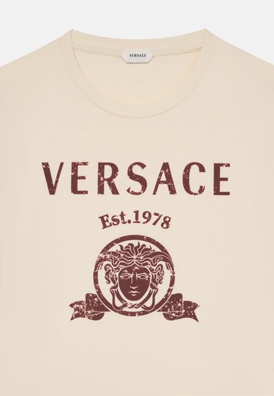 Μπεζ μπλουζάκι με μεγάλο καφέ κείμενο "VERSACE", κάτω "Est. 1978" και λογότυπο κεφαλιού Μέδουσας μέσα σε κύκλο με γραφικό κορδέλας.