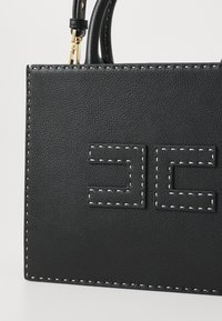 Melnas ādas soma ar baltu šuvju un izspiestu logotipu. Tai ir strukturēta forma un īsas rokturi ērtai nēsāšanai.