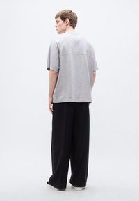 Γκρι βαμβακερό υπερμεγέθες t-shirt με κοντά μανίκια, συνδυασμένο με μαύρο παντελόνι φαρδιάς γραμμής. Απλός, μινιμαλιστικός σχεδιασμός, χωρίς ορατά σχέδια ή διακοσμητικά στοιχεία.