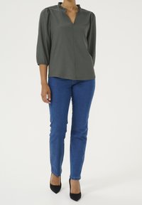Blusa grigia a maniche lunghe con colletto arricciato, abbinata a jeans skinny blu e décolleté nere a punta. Tessuto semplice, vestibilità comoda.