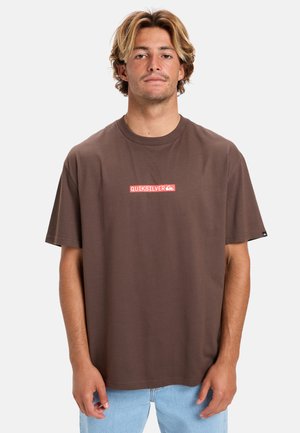 Brun bomull T-shirt med en rektangulär röd Quiksilver-logotyp på bröstet. Korta ärmar, avslappnad passform och rundad halsringning.