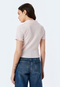 Top aderente rosa chiaro con un motivo testurizzato e ondulato e maniche corte, abbinato a jeans blu a vita alta con tasche posteriori.