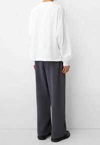 Weißer oversized Sweatshirt mit abgesenkten Schultern, kombiniert mit grauen weit geschnittenen Hosen. Glatter Stoff, minimalistisches Design und lockere Passform.