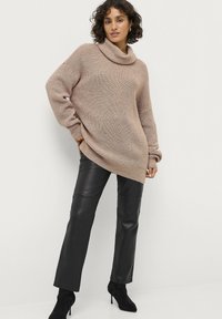 Beige strikket sweater med cowl neck, kombineret med sorte læderbukser og sorte ankelstøvler. Sweateren har en løs pasform og tekstureret mønster.
