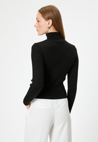 Svart ribbad polotröja med en figurnära passform och långa ärmar, med ett strukturerat stickat mönster, kombinerad med vita byxor.