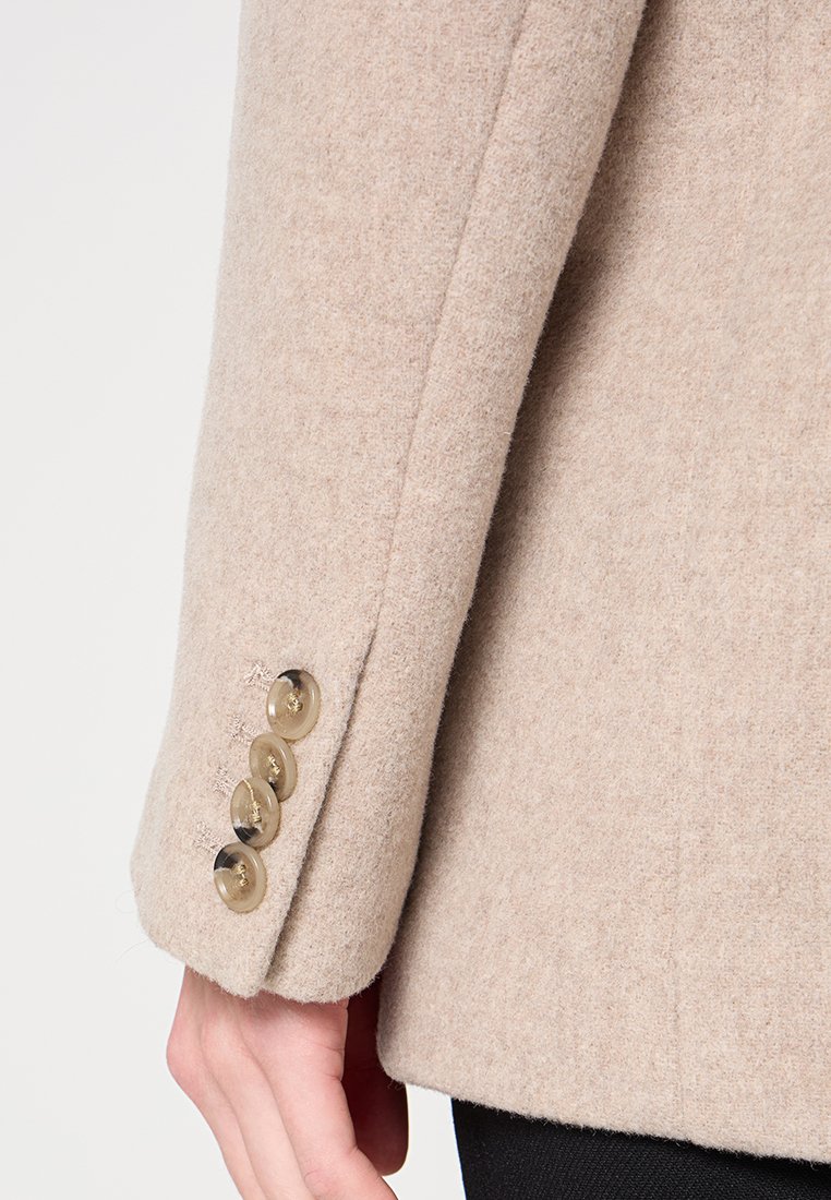 Beige Wollmischung Jacke mit geradem Schnitt, glatter Textur und vier goldfarbenen Knöpfen am Ärmel zum Schließen.