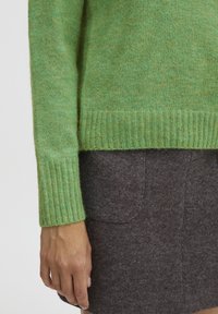 Green sweater in soft, textured wool with ribbed cuffs and hem. Paired with a dark gray felt skirt featuring two front pockets.