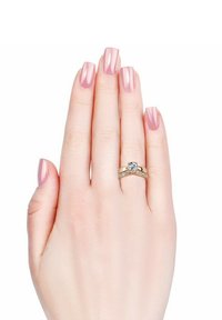 Gouden ringenset met een centrale ronde edelsteen en kleinere stenen langs een gedraaide band, tentoongesteld op een lichtbehaarde hand met roze nagels.