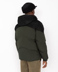 Casaco puffer em verde escuro e preto, com capuz, textura acolchoada, punhos elásticos e fechos laterais para ventilação.