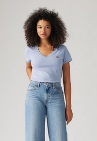 Lys blå v-hals t-skjorte i mykt stoff med lite rødt logo, kombinert med høyt liv lys blå denim jeans. Glatt tekstur, avslappet passform.