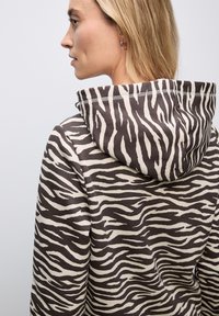 Zebra-gestreepte hoodie in bruin en crème kleuren. Voorzien van een capuchon, zachte stof en contrasterende stiksels langs de naden.