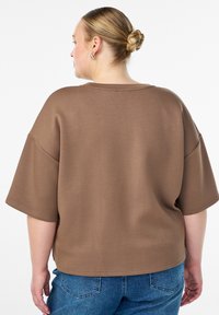 Laiad pruunist jersey-kangast top, lühikeste varrukatega ja laia kaelusega. Selg on puhta viimistluse ja peente õmblusdetailidega. Kombineeritud siniste teksadega.