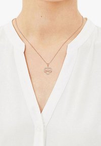 Roségoldkette mit einem herzförmigen Anhänger, der ein Unendlichkeitssymbol und kleine klare Edelsteine rund um den Rand zeigt. Die Kette ist filigran.