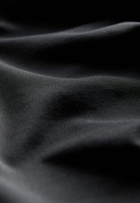 Közeli kép sima, fekete szövetről, melynek lágy redői és finom, átlós bordázott mintázata van gyengéd megvilágítás alatt.